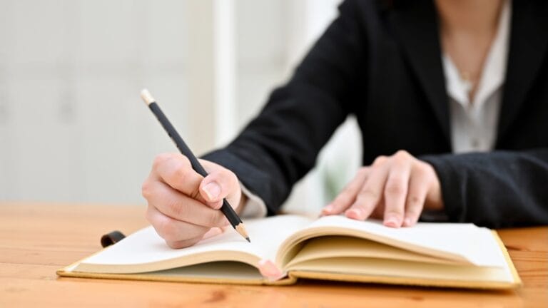 Wniosek o ustalenie kontaktów z dzieckiem - jak napisać i co musi zawierać? Osoba pisząca wniosek o ustalenie kontaktów z dzieckiem przy biurku w notesie.